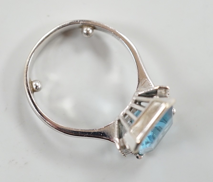 A 750 white metal and emerald cut blue topaz set dress ring, with diamond chip set borders, size O, gross weight 7.8 grams.